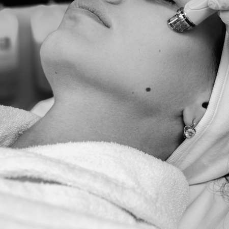 Beautiful young girl receiving ultrasound face cleansing in beauty salon, black and white imageの写真素材