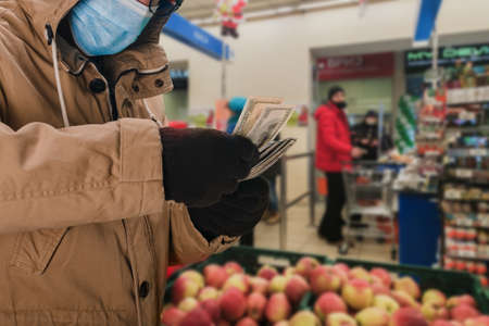 Portrait of man in safety medical mask holding big cash money pack, elderly people during a pandemicの写真素材