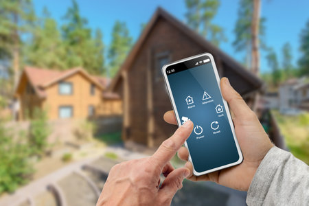 Male hands with smart home menu icons on digital smartphone screen over country cottage backgroundの写真素材