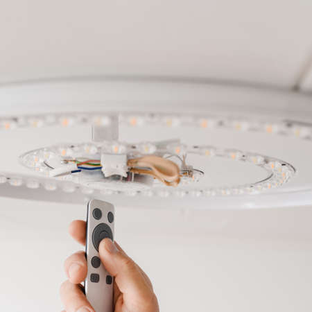 Man with remote control adjusting brightness of led lamp after repairの写真素材