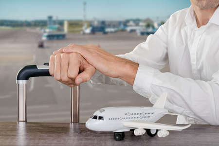Closeup photo of unrecognizable businessman sitting by window at airport with luggage and waiting for departureの写真素材