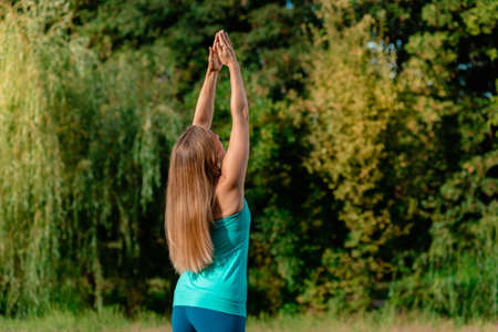 Slim fit sportswoman stretching her hands in park on sunset