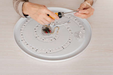 Close-up of a male engineer repairing or replacing a ceiling diode lamp with a screwdriver in his...