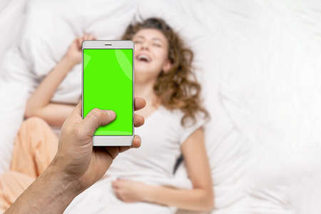 Man taking picture of smiling woman in bed with smartphone and sharing in social networkの写真素材