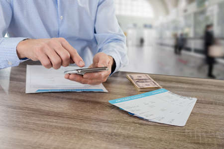 Young man with smartphonne and cash money counting travel expenses before journeyの写真素材