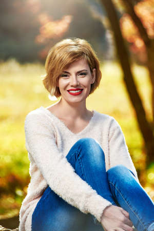 Portrait of pretty cheerful woman posing in park on sunny autumn day