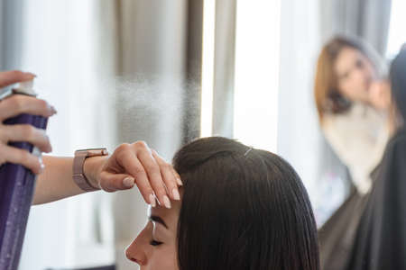 Professional stylist using hair spray to fix modern hairstyleの写真素材