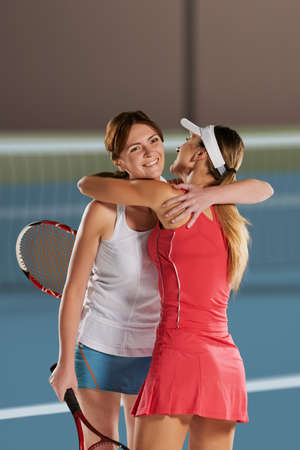 Portrait of two happy young sportswomen hugging on tennis courtの写真素材