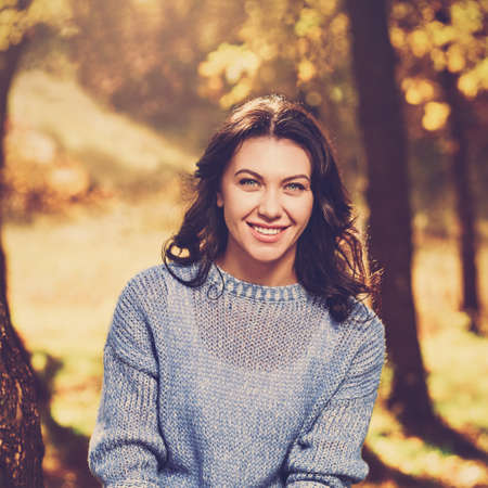 Beautiful young smiling girl posing in warm autumn forestの写真素材