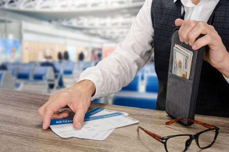 Young businessman waiting in airport terminal with tickets and money in hands