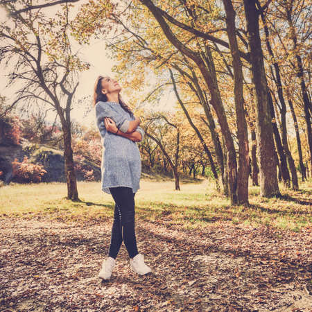 Young stylish girl having walk in autumn park on sunny dayの写真素材