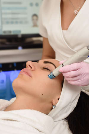 Beautiful young girl receiving ultrasound face cleansing in beauty salonの写真素材