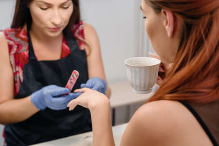Professional manicurist filing nails of young woman in spa salon