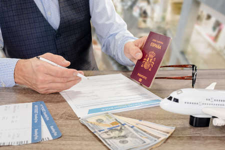 Young businessman with international passport and avia ticket filling insurance form before trip, nscription European Union Spain passportの写真素材
