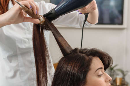 Closeup of professional hairdresser using dryer and brush while working with female customerの写真素材