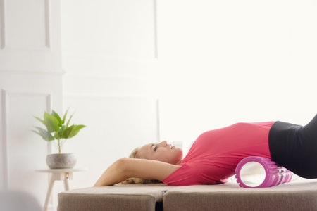 Young fit woman in sportswear massaging body during training at homeの写真素材