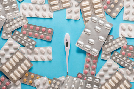 Digital thermometer and medical pills for virus treatment on blue background