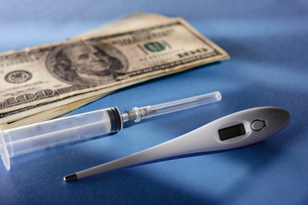 Composition of medical syringe, electronic thermometer and money cash on blue backgroundの写真素材