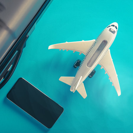 Flight suitcase with smartphone and model of airplane isolated on blue backgroundの写真素材