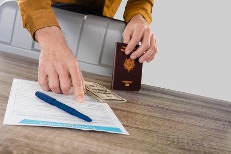 Man with currency notes and french passport reading insurance application form in the studio on a light gray backgroundの写真素材