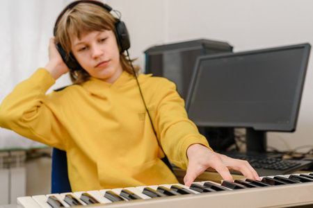Relaxed teen boy with headphones playing music on synthesizer at home studioの写真素材
