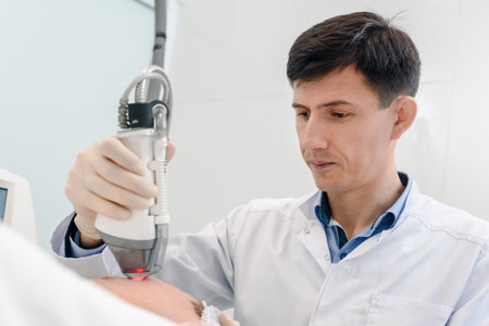 Handsome male cosmetologist doing laser exfoliation treatment in beauty salon