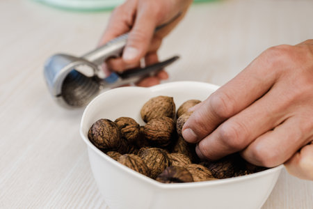 Man with nutcracker taking walnuts from white bowl