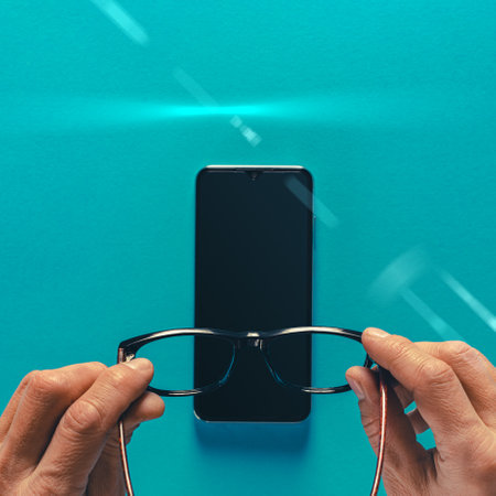 Male hands holding glasses and modern smartphone on blue backgroundの写真素材