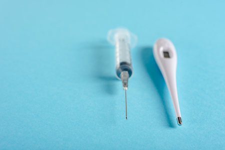 Medical disposable syringe and digital thermometer isolated on blue backgroundの写真素材