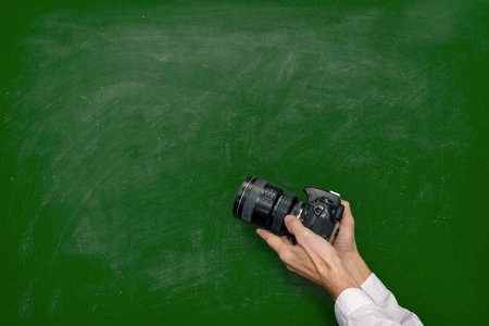 Closeup photo of man holding digital camera against green chalkboard with space for textの写真素材