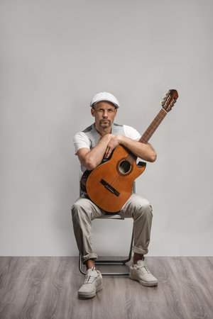 Stylish handsome man in flat cap and waistcoat posing in studio with classical guitarの写真素材