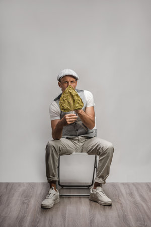 Stylish modern man sitting on chair and covering face with leaf of withered plantの写真素材