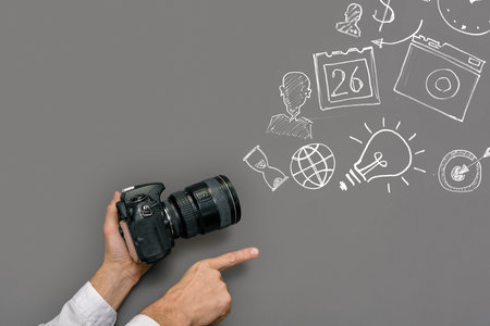 Man with camera pointing finger forward and drawn investment business symbols on gray chalkboard