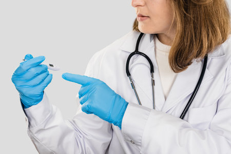 Professional female pharmacist with thermometer working on studio gray background