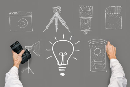Male hand holding professional camera on gray chalkboard background with handdrawing illustrationsの写真素材