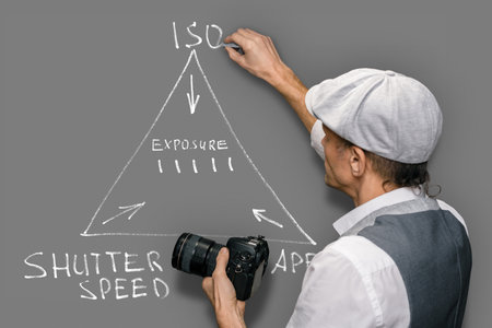 A professional male photographer teaches to take pictures, draws an exposure scheme, ISO aperture shutter speeds on a gray backgroundの写真素材