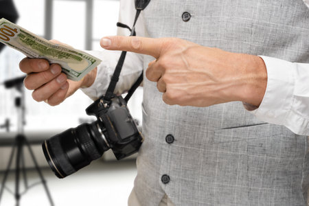 Closeup photo of man with modern digital camera posing with dollar currency in photo studio, The studio is well-lit, with various photography equipment visible in the backgroundの写真素材