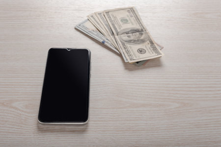 Smartphone and cash on wooden table, internet banking app concept