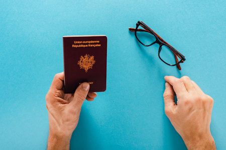 Closeup of man tourist holding french passport and glasses isolated on blue backgroundの写真素材