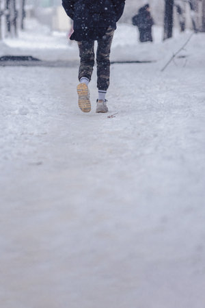 A man in summer sneakers walks along a slippery sidewalk during a snowfallの写真素材