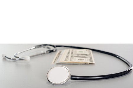 a stethoscope goes around several dollar banknotes on a gray table with copy space backgroundの写真素材