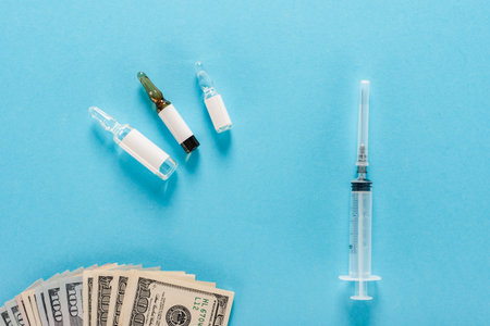 Syringe, ampoules for injection and dollar banknotes lying on blue backgroundの写真素材