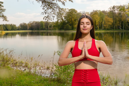 Portrait of attractive young girl in lotus pose feeling zen-like in city park, Outdoor yoga by the lake in a serene parkの写真素材