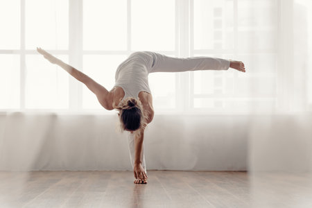 Young athletic woman practicing yoga with big light window on the background, Captivating image of a...