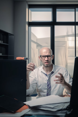 Young unlucky businessman doing self first aid after computer fix, Unlucky day at the office: Businessman provides self-first aidの写真素材