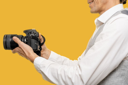 Closeup of young man with modern camera work as photographer on yellow background, he seamlessly blends the classic art of photography with the advancements of the digital age.の写真素材