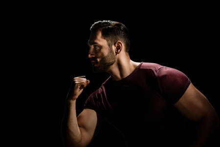 Portrait of brutal sporty strong guy with modern hairstyle isolated on black background, Low-key allure: A dramatic portrait of a dark, young man with a beardの写真素材