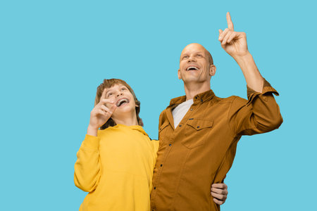 Portrait of happy father and son having fun together, pointing away and smiling, Playful father-son duo have a blast, pointing in excitement and beaming with delight.の写真素材