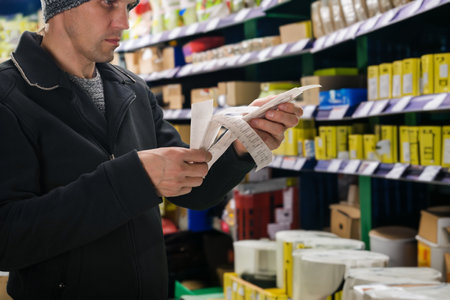 Adult man holding receipt with high prices from hardware store and looking upset. Checkout success: Hardware store purchase paid for, receipt in handの写真素材