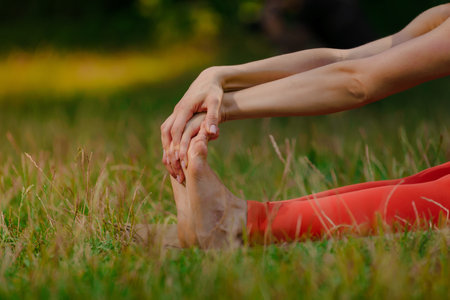 Closeup of young woman flexing feet while stretching on yoga mat outdoor. Solo stretch: Young woman finds solace stretching legs in lush park.の写真素材